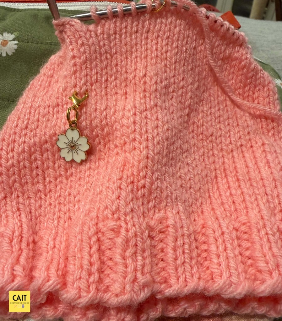 Pink knit hat in progress atop a green project bag.